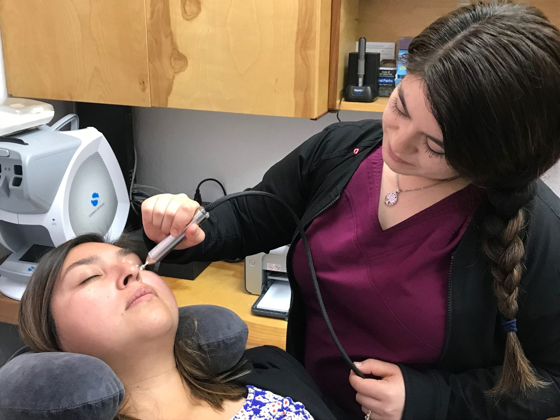 A technician performing an in-office dry-eye treatment on a reclined patient