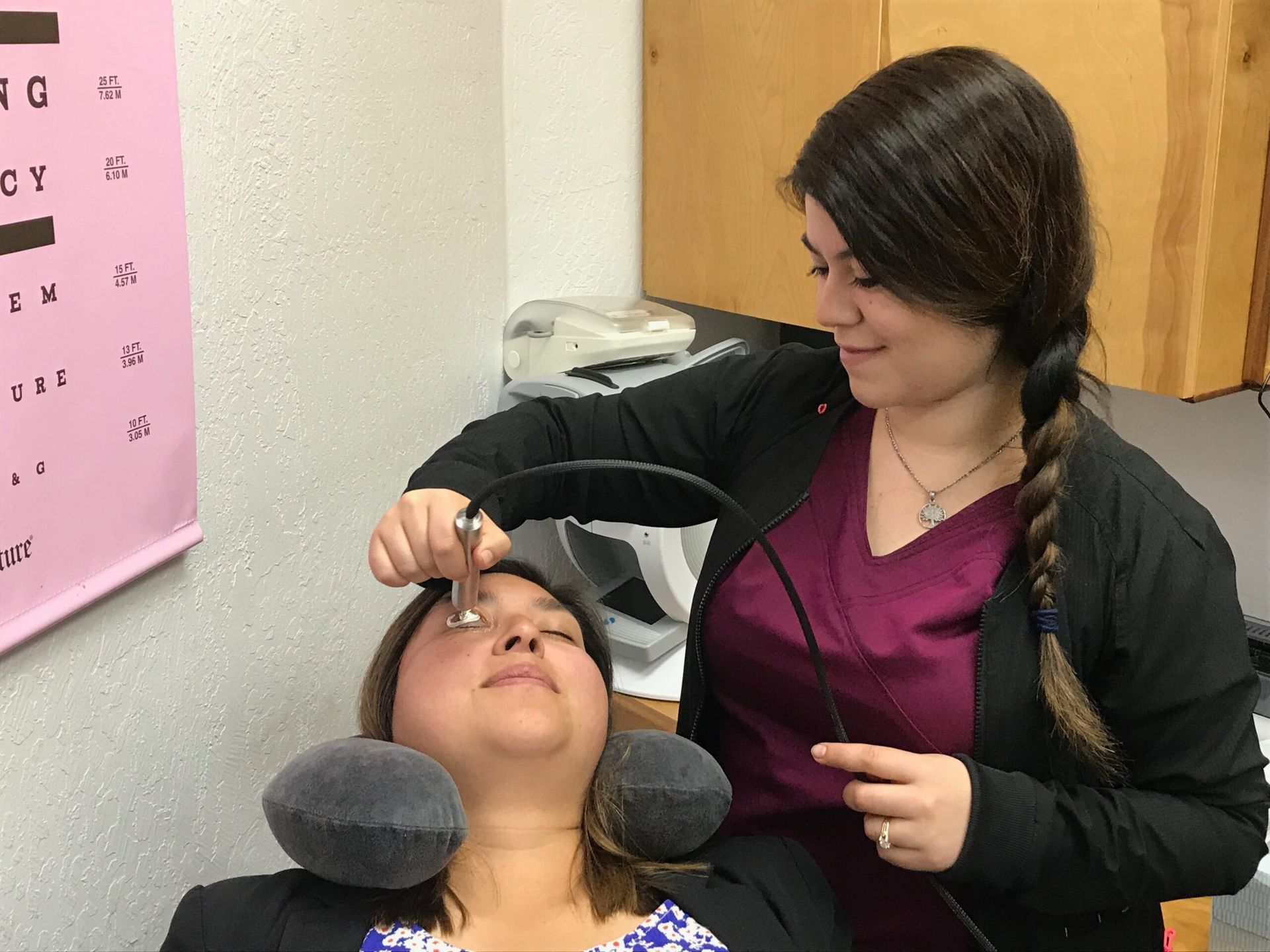 A technician performing an in-office eyelid treatment on a reclined patient
